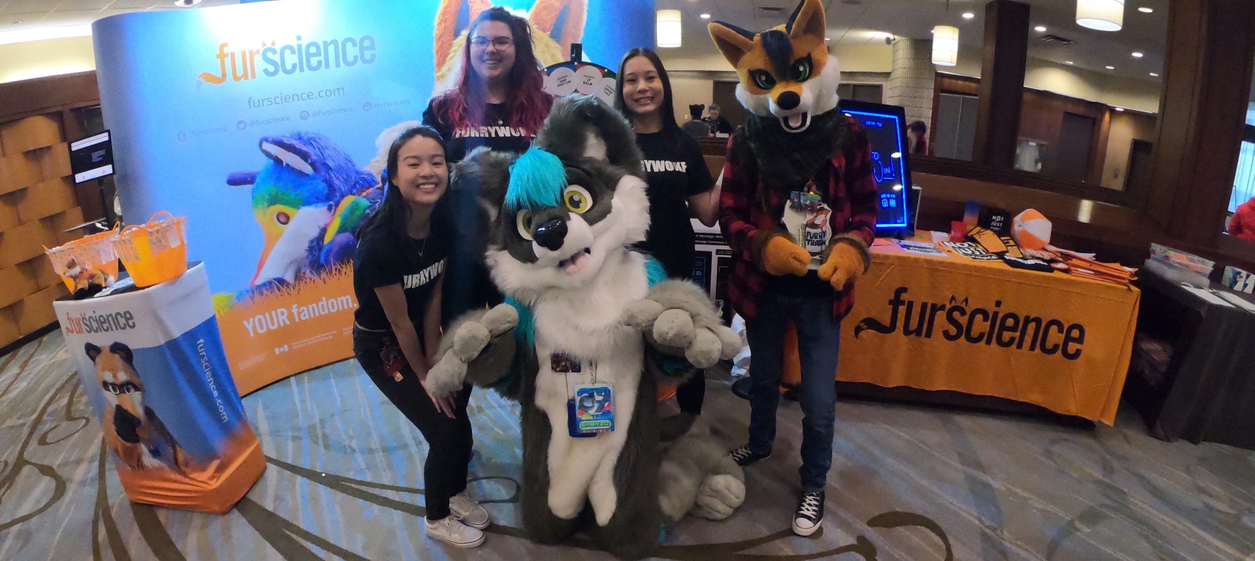 Furscience Research Assistants pose in front of the Furscience Booth with furry attendees in fursuits at Furnal Equinox, a furry convention in Toronto, Ontario, Canada